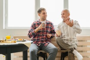 son,and,senior,father,sitting,on,chairs,indoors,at,home,